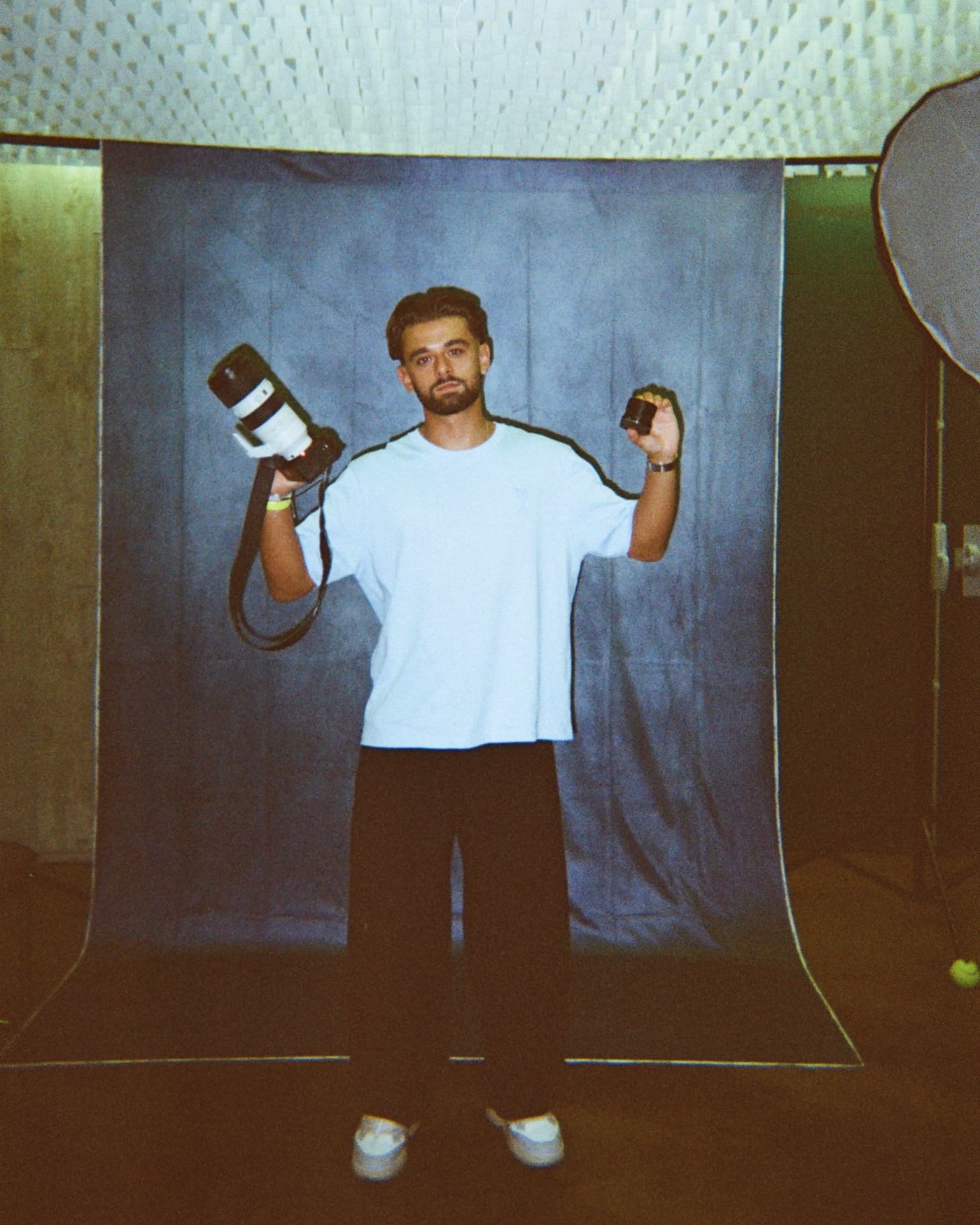 ALEH, photographe, devant un fond bleu en studio avec sa caméra et son objectif